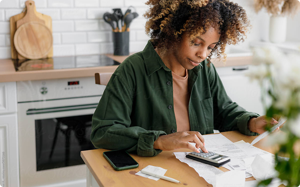 Person in a green shirt uses a calculator to sort white receipts and a card on a wooden kitchen table.